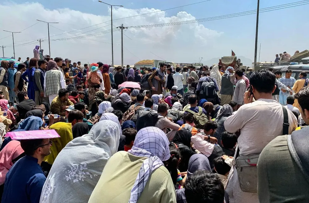 Afganos se reúnen a lo largo de una carretera mientras esperan para abordar un avión militar estadounidense para salir del país, en un aeropuerto en Kabul el 20 de agosto de 2021