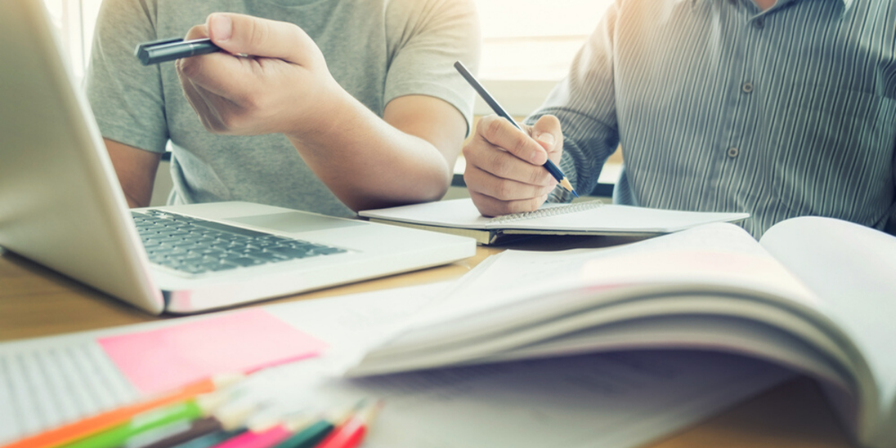 Dos personas aprendiendo inglés con su computadora y cuadernos