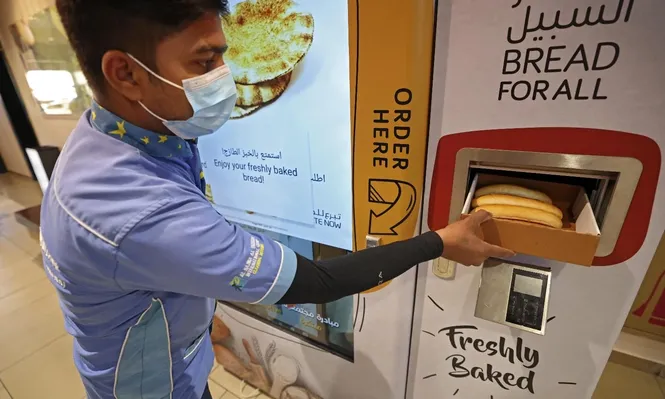 Un hombre recoge artículos de una máquina expendedora que reparte pan gratis, en Dubái.