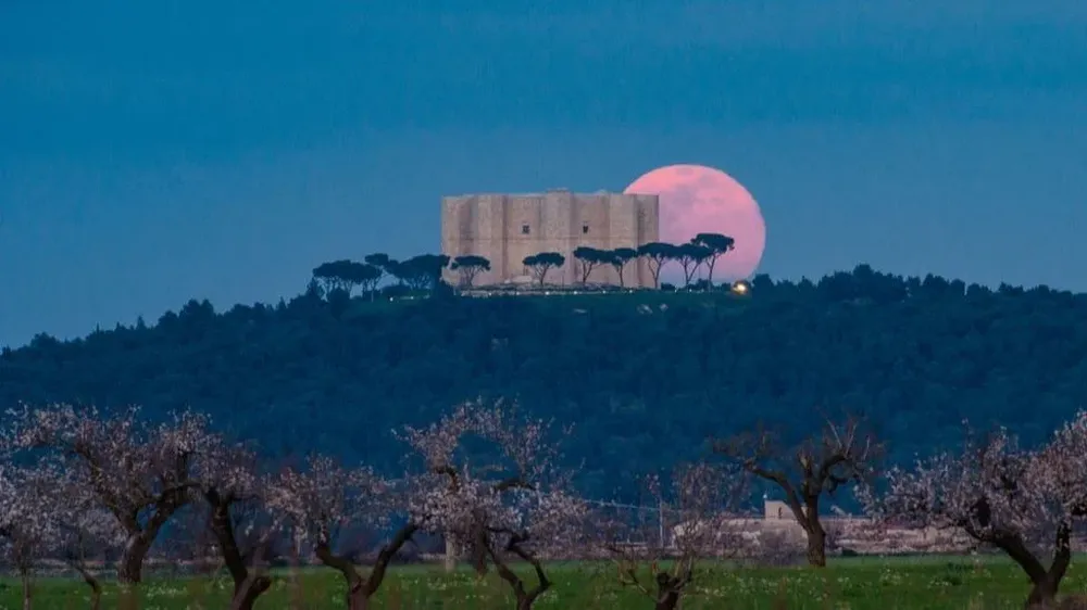 La luna llena sale detrás del Castel del Monte en Andria, Italia