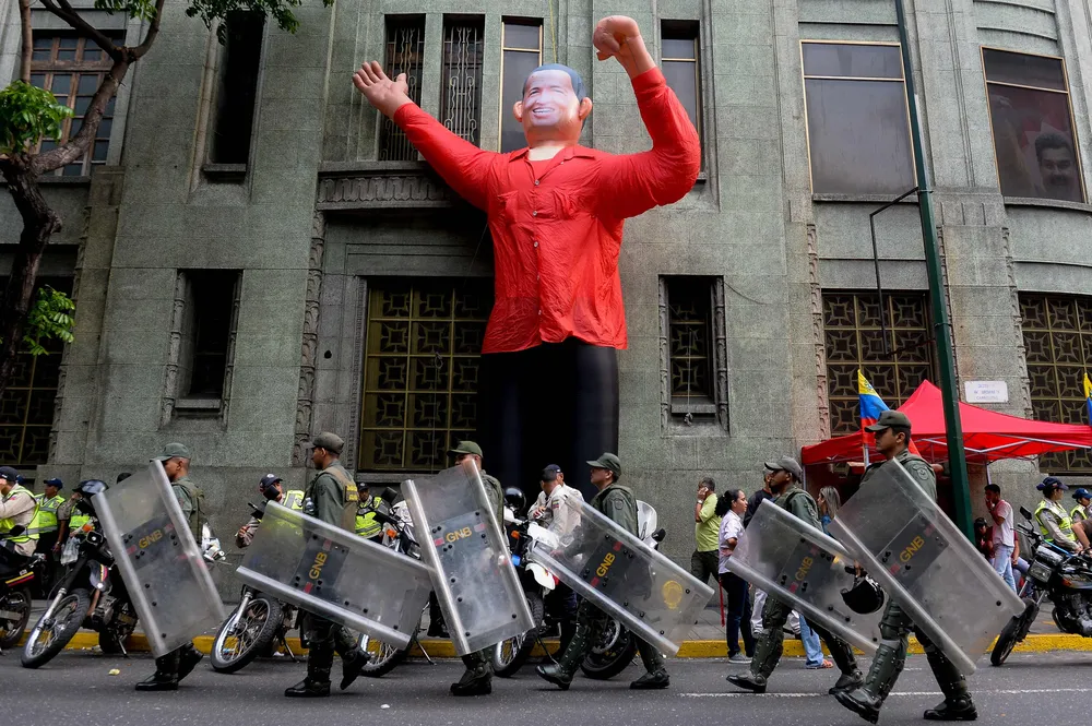 Members of the National Guard walk in front of an inflatable doll depicting late President Hugo Chavez during a demonstration at Miraflores presidential palace in Caracas on April 14, 2016. Supporters of Venezuelan President Nicolas Maduro mobilized to ask him to block a law granting titles of property of the Mision Vivienda promoted by the opposition. / AFP / FEDERICO PARRA