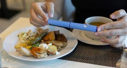 Una mujer con una dosis de Ozempic junto a un plato de comida y una taza de sopa.