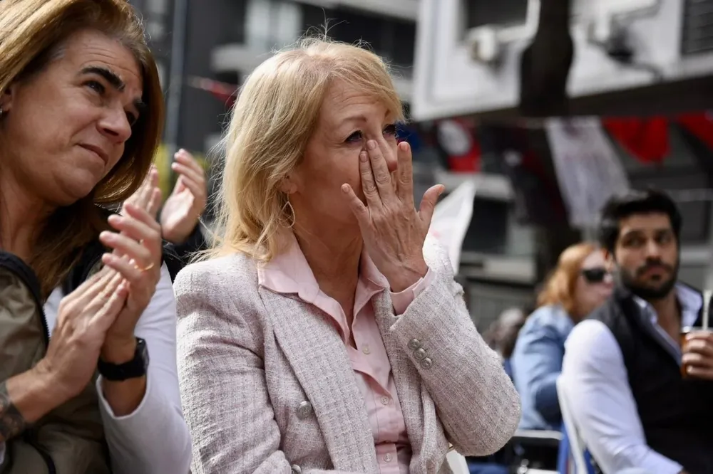 Acompañada por Silvia Nane, Carolina Cosse se ve emocionada después de que Marcelo Abdala citara a Tabaré Vázquez en el acto por el Día de los Trabajadores; en el fondo de ver al precandidato colorado Andrés Ojeda