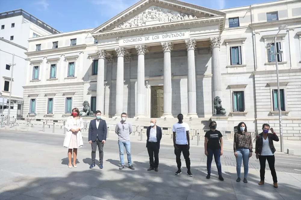 El trabajador migrante y miembro del movimiento #RegularizaciónYa Seydou Diop (4d); la portavoz de #RegularizaciónYa, Edith Espínola (3d); la diputada de Unidas Podemos Isabel Franco (2d); el portavoz de ERC en el Congreso de los Diputados, Gabriel Rufián (2i); y la portavoz de JxCat en el Congreso de los Diputados, Laura Borràs (1i); entre otros miembros del Congreso, posan frente al Congreso de los Diputados.