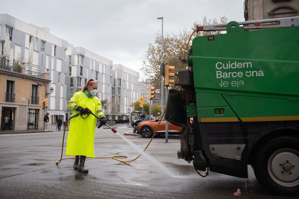 Una trabajadora de la limpieza riega una calle con una manguera en Barcelona