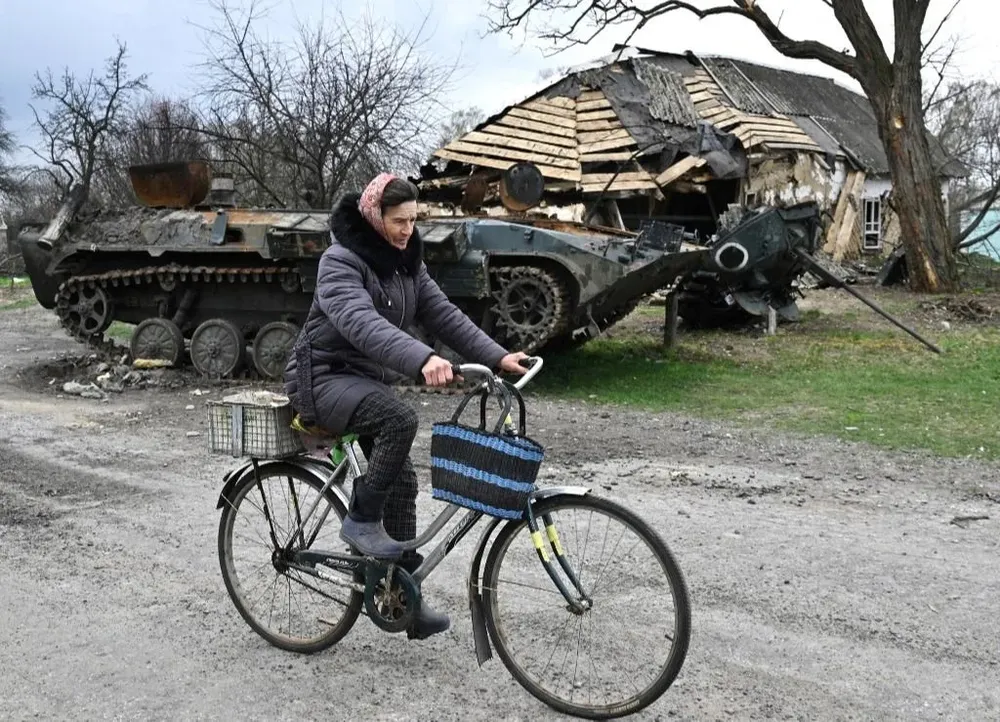 Una mujer monta su bicicleta frente a un vehículo blindado de transporte de personal (APC) destruido en la aldea de Rusaniv, en la región de Kiev.