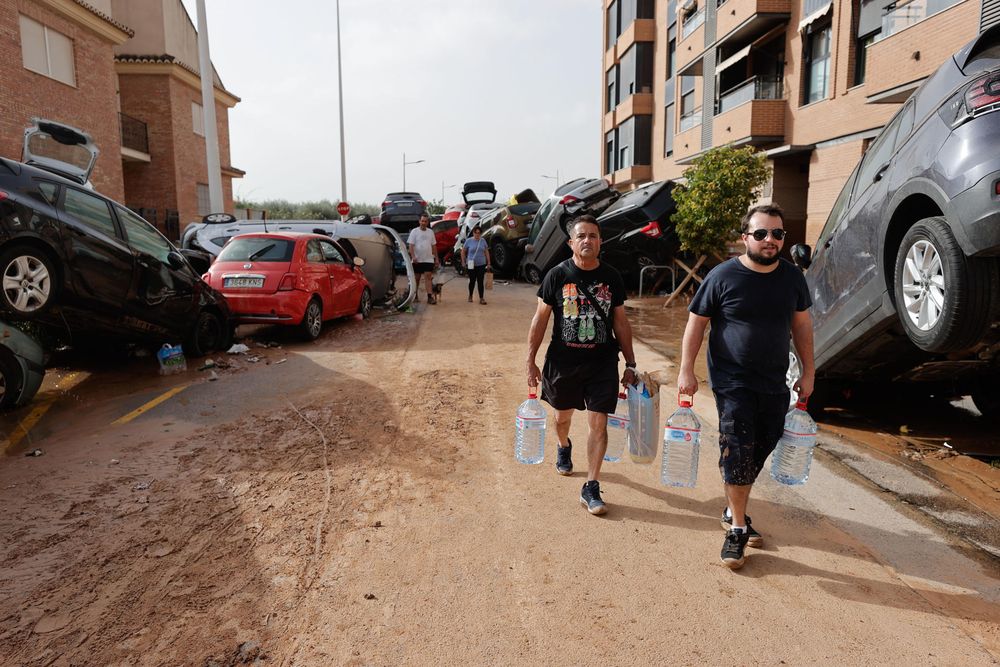 Personas con botellas de agua caminan entre los vehículos destrozados en la región valenciana de Paiporta. EFE