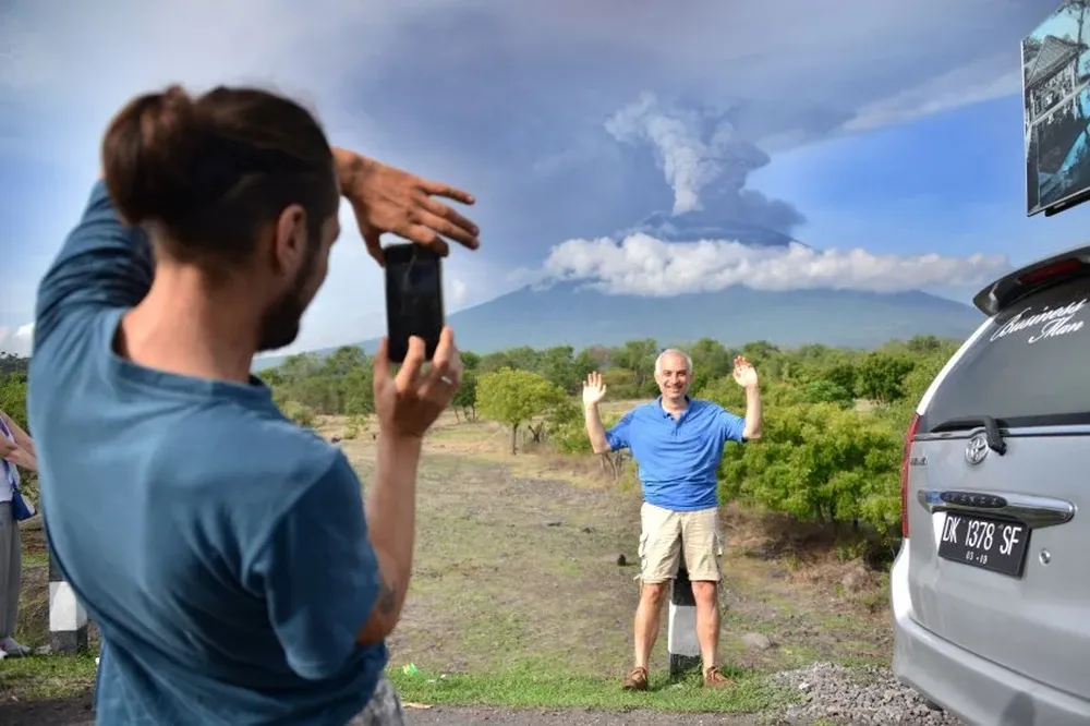 Un turista extranjero se toma una foto con el Agung en actividad detrás suyo, en la isla de Bali, Indonesia. Una erupción puede ser inminente mientras se amplía la zona de exclusión.