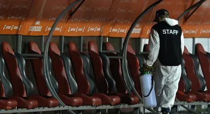 Un funcionario desinfectando el sector de los suplentes de un estadio