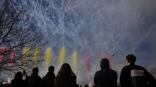 Varias personas observan el humo de colores durante la primera mascletà madrileña, en el Puente del Rey de Madrid Río.