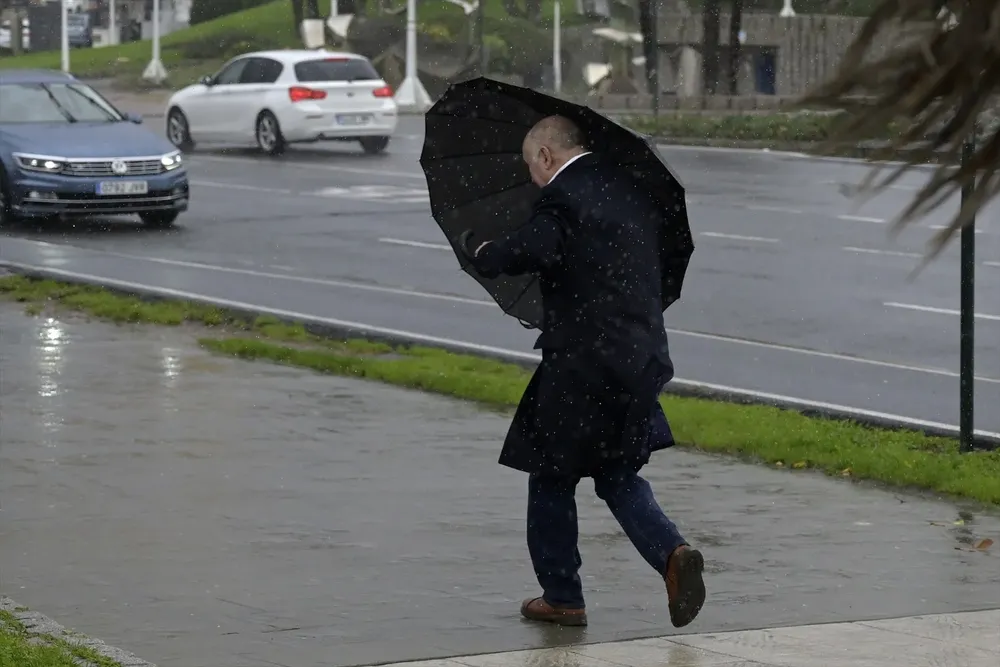 Un hombre con paraguas trata de refugiarse del viento y de la lluvia en A Coruña, Galicia.