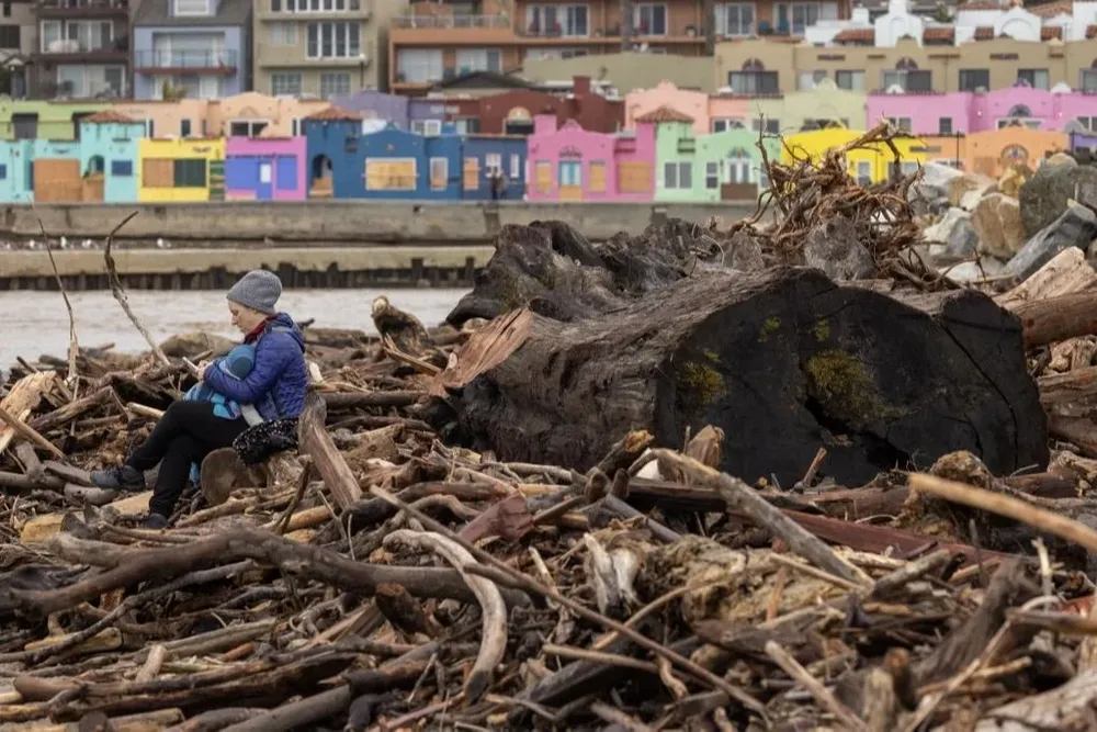 Una madre y un niño se sientan sobre un árbol desplazado por las tormentas que azotaron a California