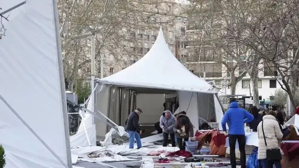 Varias personas recogen piezas del suelo tras volarse las carpas ubicadas en la Feria de la Artesanía de Valladolid