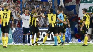 Maximiliano Olivera le entrega al árbitro Ostojich una petaca de vidrio que cayó desde la tribuna cuando el lateral aurinegro intentaba reponer un lateral