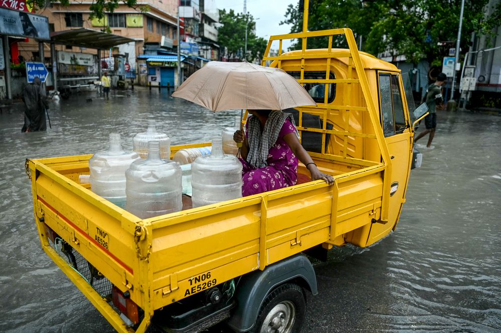 Una mujer que sostiene un paraguas viaja en un vehículo a través de una calle inundada en medio de fuertes vientos y lluvias en Chennai el 30 de noviembre de 2024, antes de que toque tierra el ciclón Fengal en el estado indio de Tamil Nadu.