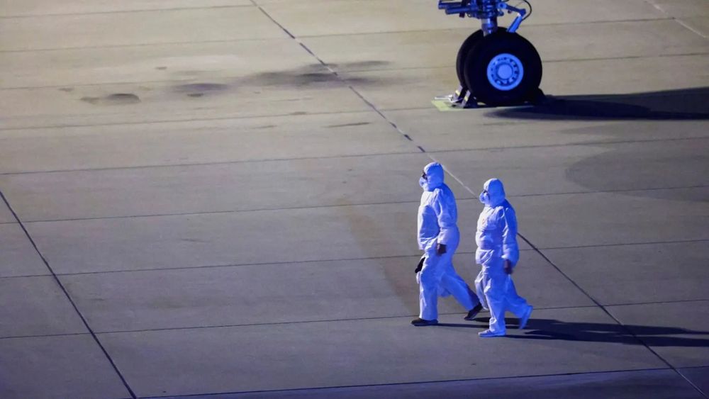 Personal con trajes de protección camina cerca de un avión que transporta pasajeros evacuados.