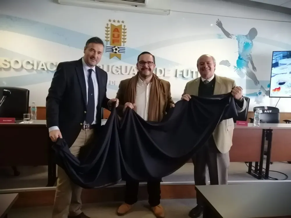 Romeo Volonté (SUL), Juan Ignacio Buffa (MGAP) y Fabio Montossi (INIA) muestran la tela con la que se confeccionarán los trajes.