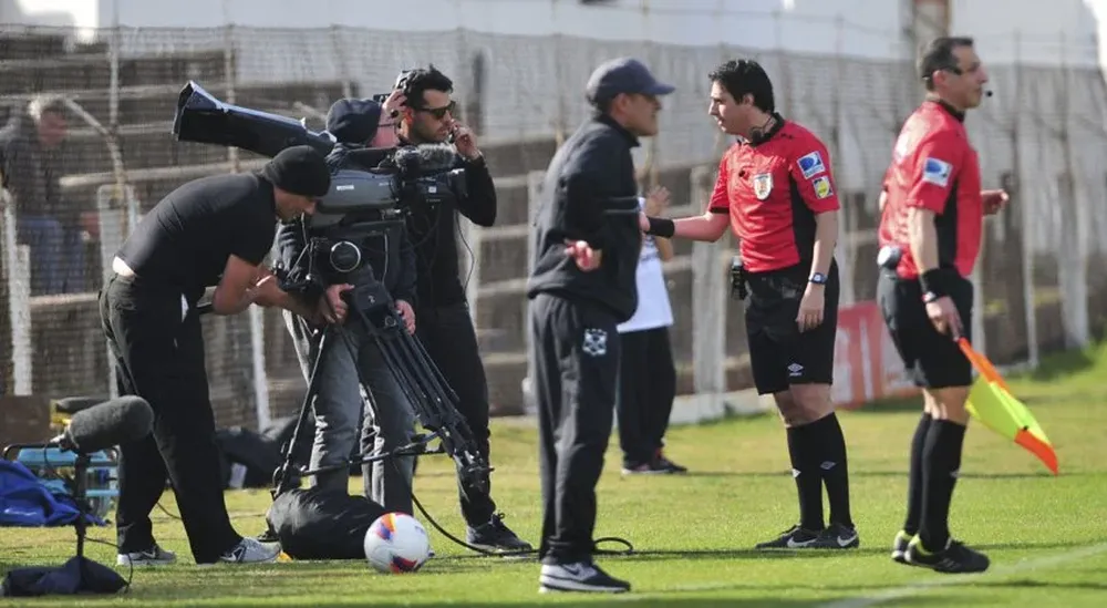 El cuarto árbitro Adrián Sánchez solicita al camarógrafo, correr su cámara hacia atrás para permitir la labor del primer asistente Carlos Pastorino