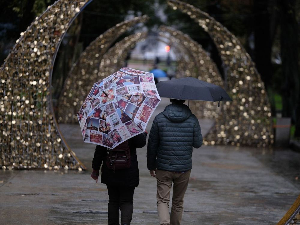 Una pareja pasea con paragüas en una calle decorada por las fiestas de fin de año