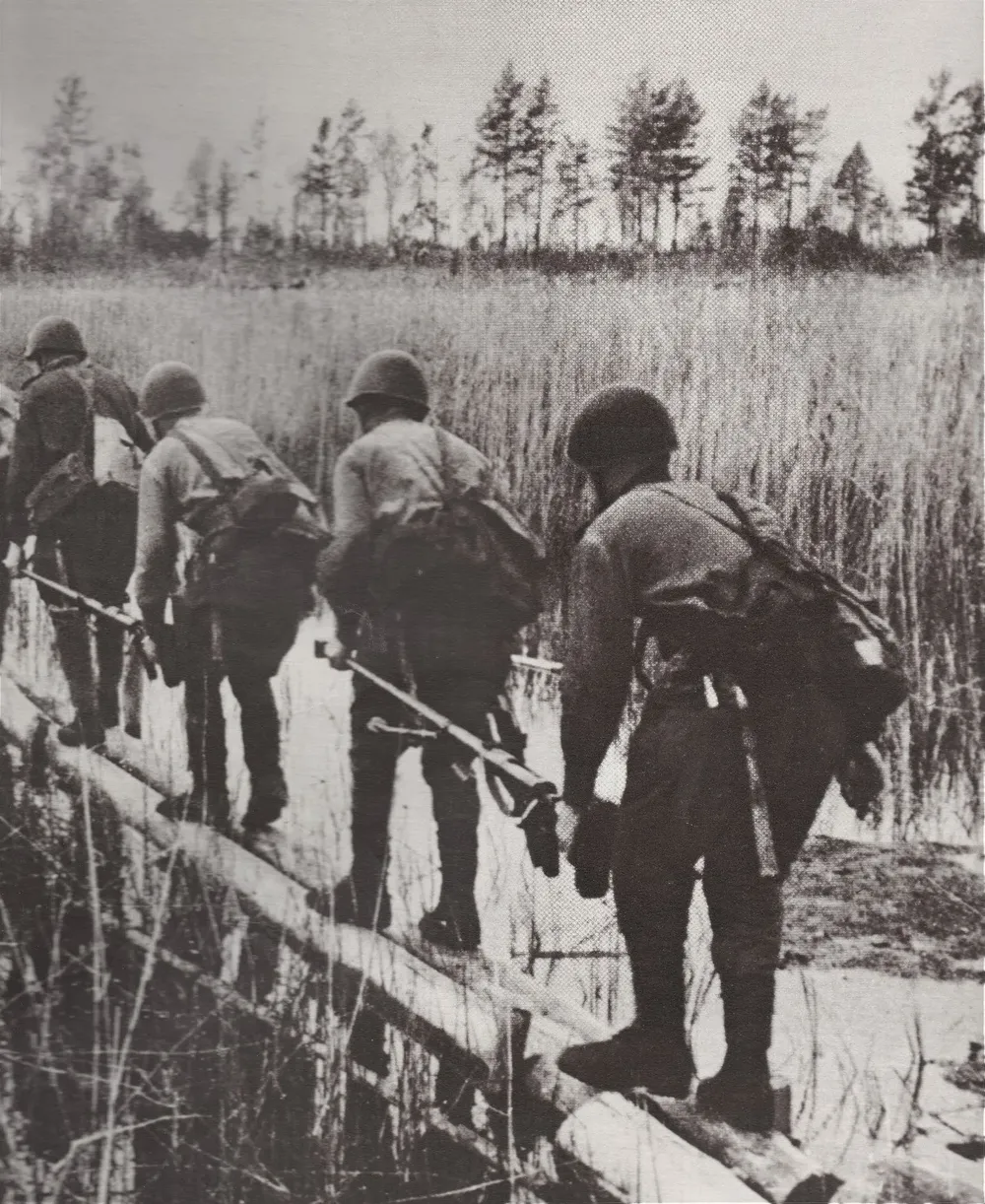 Soldados soviéticos cruzan un bañado sobre un estrecho puente de troncos en el verano de 1944, en su ofensiva sobre Finlandia