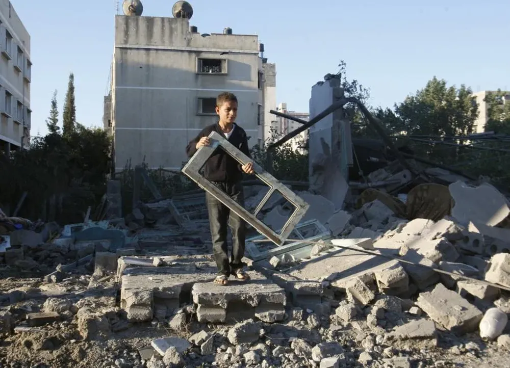 Niño palestino sostiene un vidrio de la ventana de casa dañada en un ataque israelí en Gaza