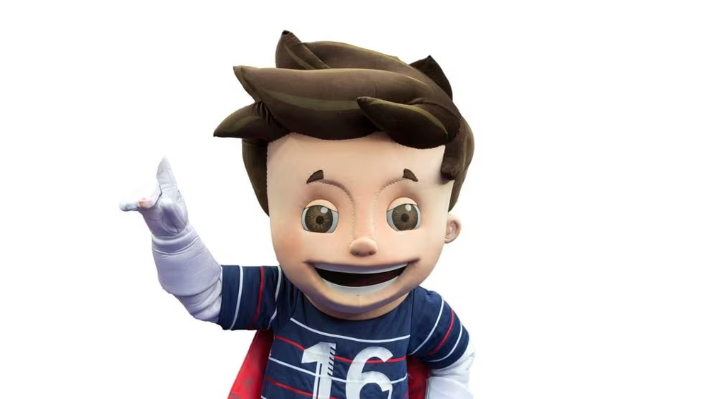 Super Víctor (Francia 2016): Super Víctor posa con su balón mágico y su capa estampada con los logos de la Eurocopa, simbolizando el espíritu jovial del fútbol francés.