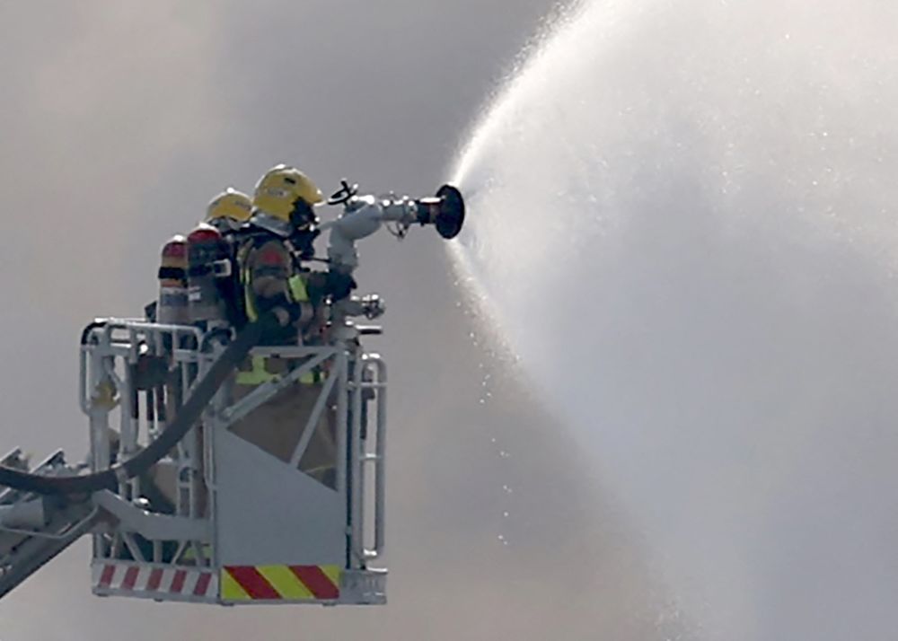 España: bomberos en una plataforma usan un aerosol para extinguir un incendio mientras el humo sale de un edificio que almacena productos de limpieza para piscinas, en la ciudad costera de Vilanova i la Geltru, al sur de Barcelona.