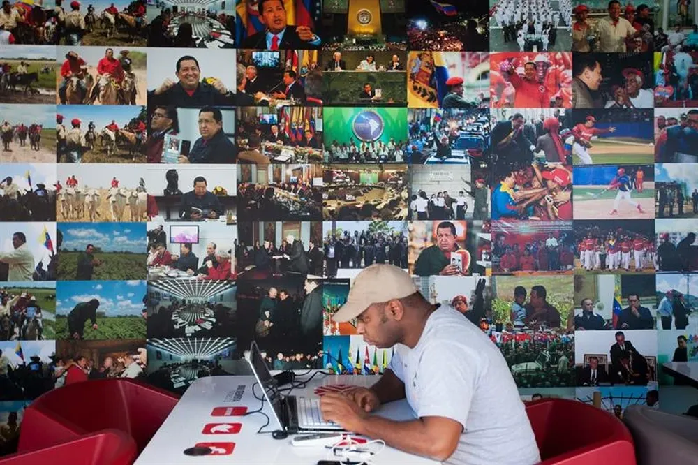 Venezuela- Un hombre usa un computador frente a fotografías en una exposición sobre Hugo Chavez