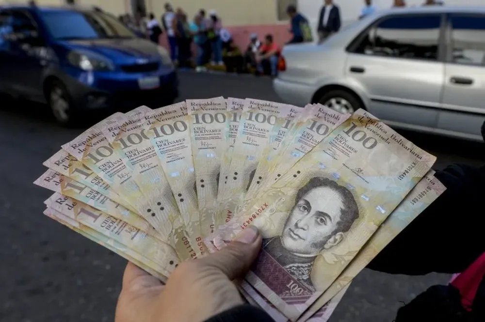 Un hombre muestra billetes de 100 bolívares mientras hace cola afuera del Banco Central de Venezuela para cambiarlos