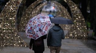 Una pareja pasea con paragüas en una calle decorada por las fiestas de fin de año