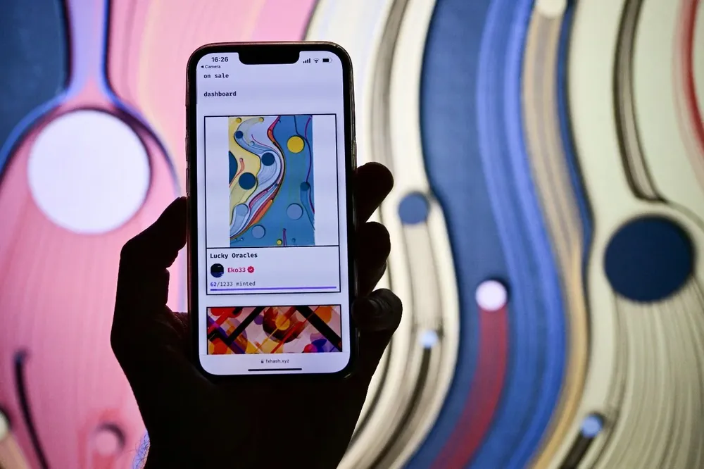 Un visitante sostiene un teléfono celular que muestra una obra de arte virtual vendida por NFT durante un día de vista previa de Art Basel, la principal feria de arte moderno y contemporáneo del mundo en Basilea.
