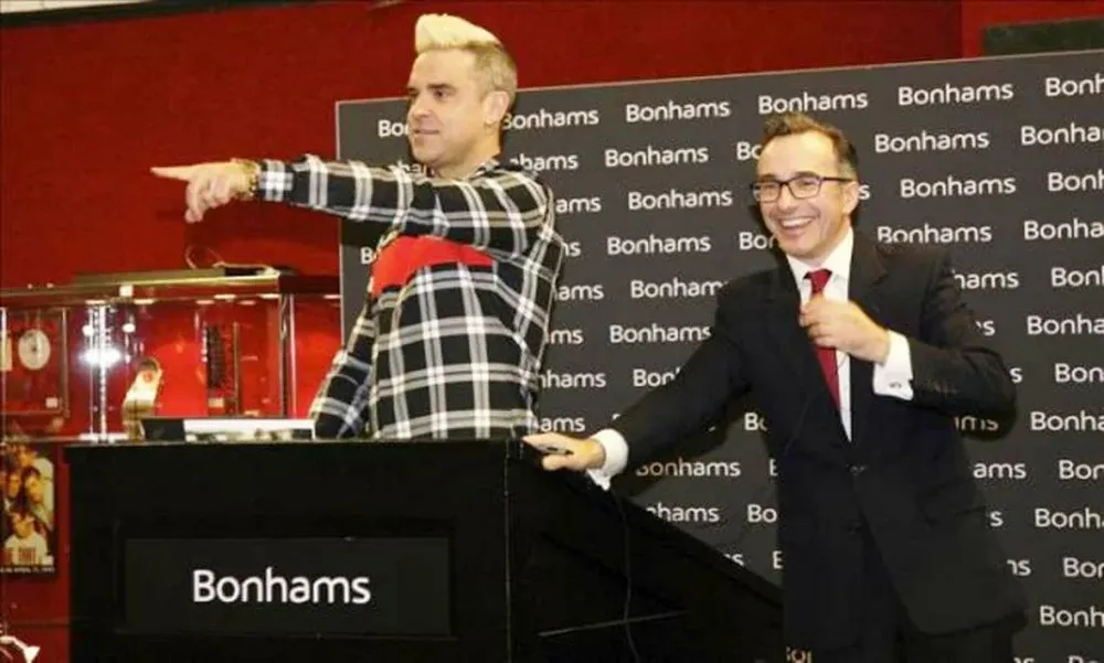 El cantanto británico Robbie Williams junto al rematador James Stratton, durante la puja Doing It For The Kids (Haciéndolo por los niños), en Londres, Reino Unido