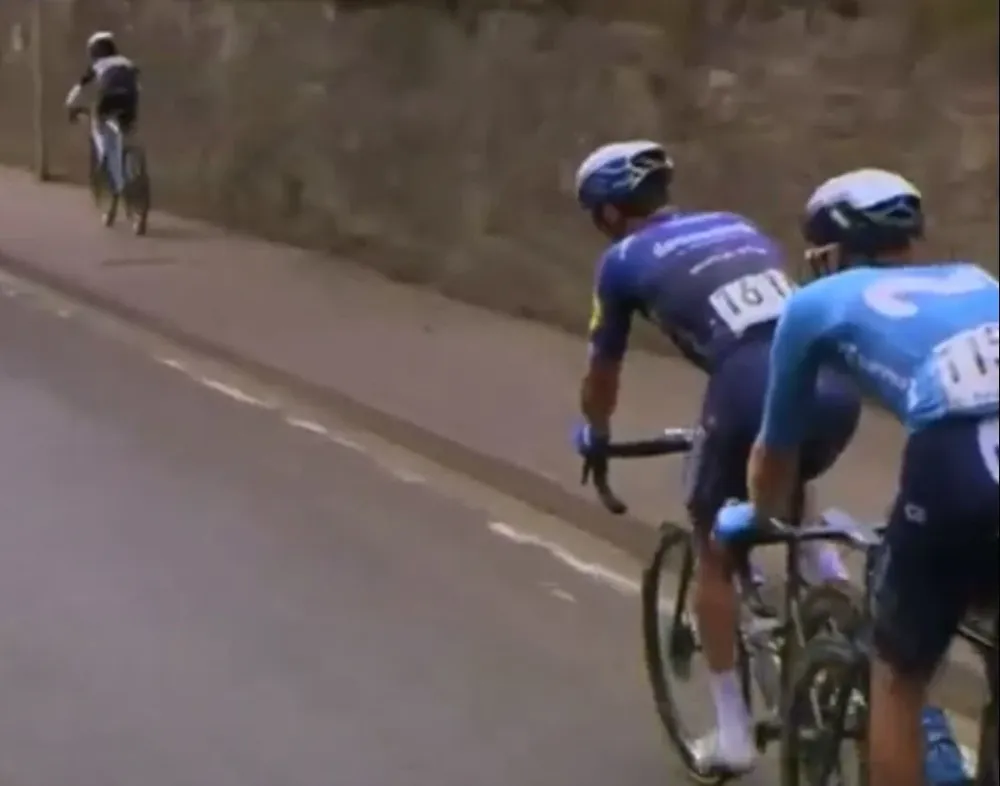 El niño pedalea por la vereda marcándole el ritmo a los profesionales van por la calle en el Tour Británico