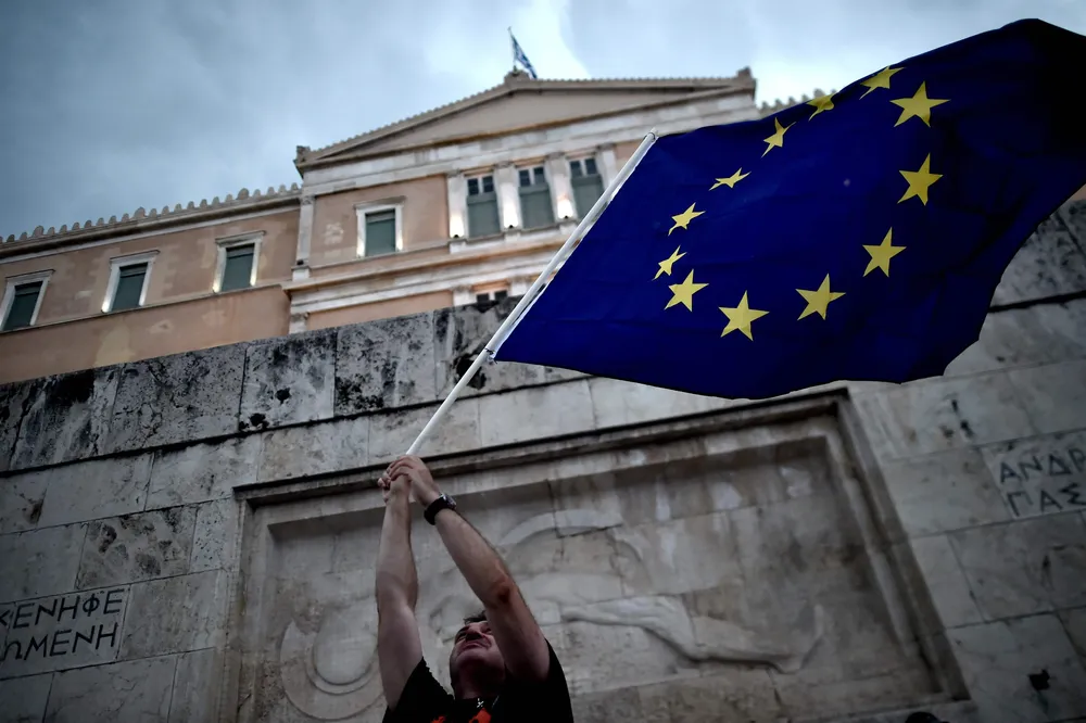 (FILES) In this file photo taken on June 30, 2015 a pro-European Union protester waves an EU flag during a demonstration in front of the parliament in Athens. After nearly a decade of stringent and hugely unpopular austerity measures to stabilise its economy, Greece on August 20, 2018 exits the EU-IMF bailout programmes agreed to prevent it from crashing out of the eurozone. / AFP / ARIS MESSINIS