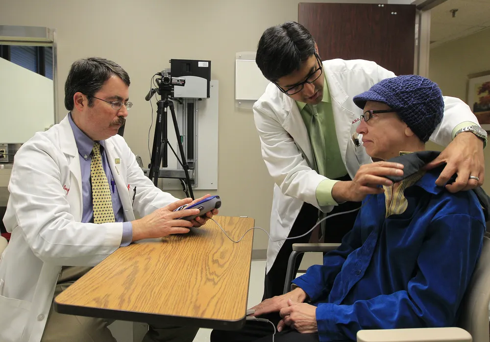 Los doctores Doug Scharre (izquierda) y Punit Agrawal (centro) preparan el dispositivo de estimulación cerebral para monitorear a la paciente Kathleen Sanford