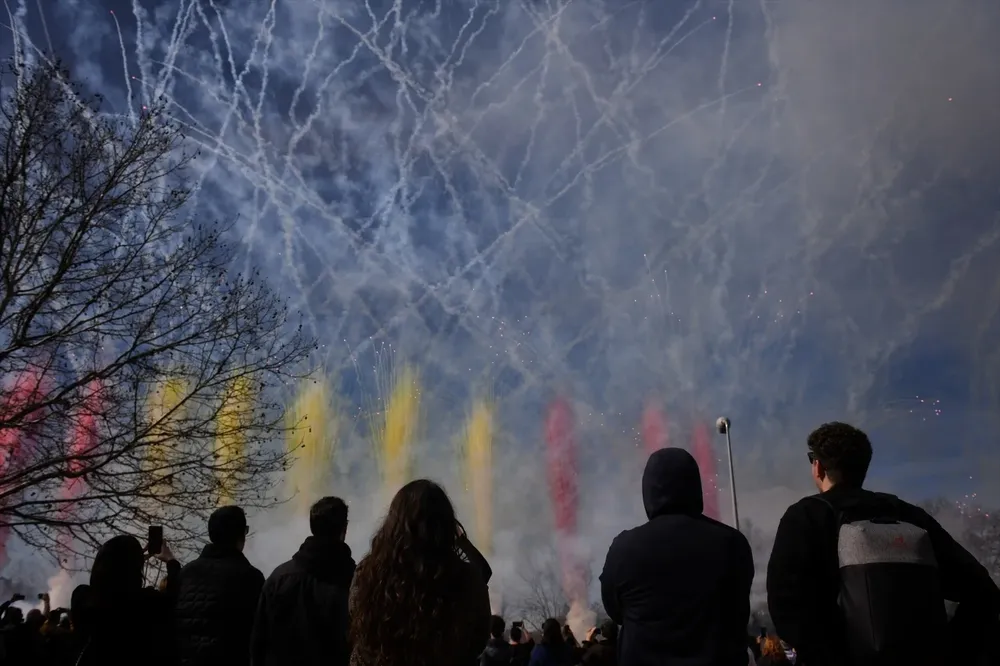 Varias personas observan el humo de colores durante la primera mascletà madrileña, en el Puente del Rey de Madrid Río.