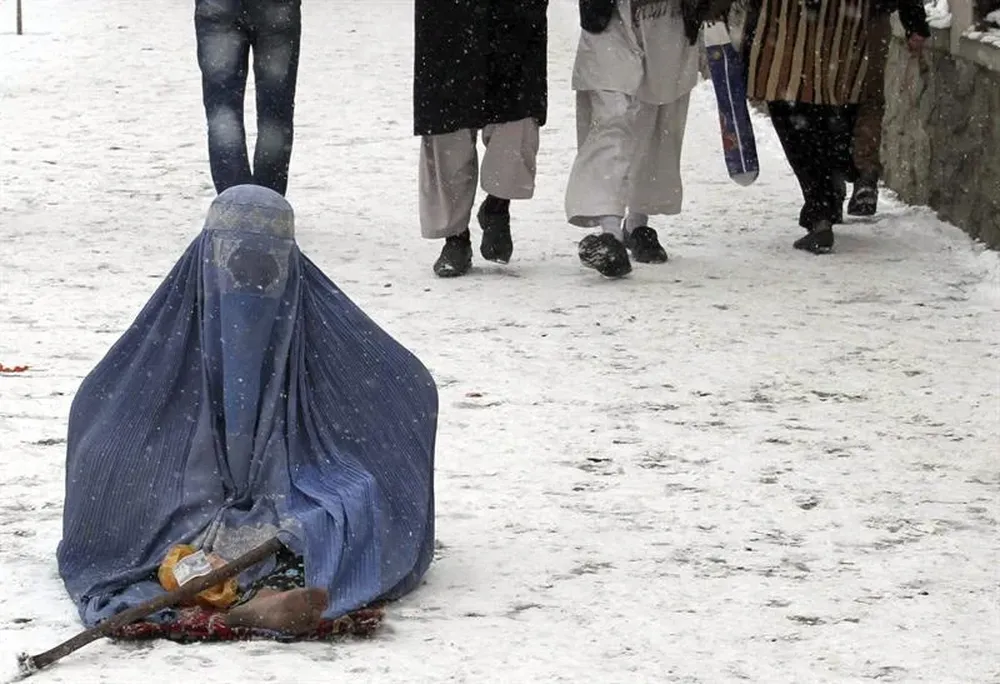 Afganistán- Una mujer cubierta por un burka pide limosna en una calle cubierta de nieve en Kabul