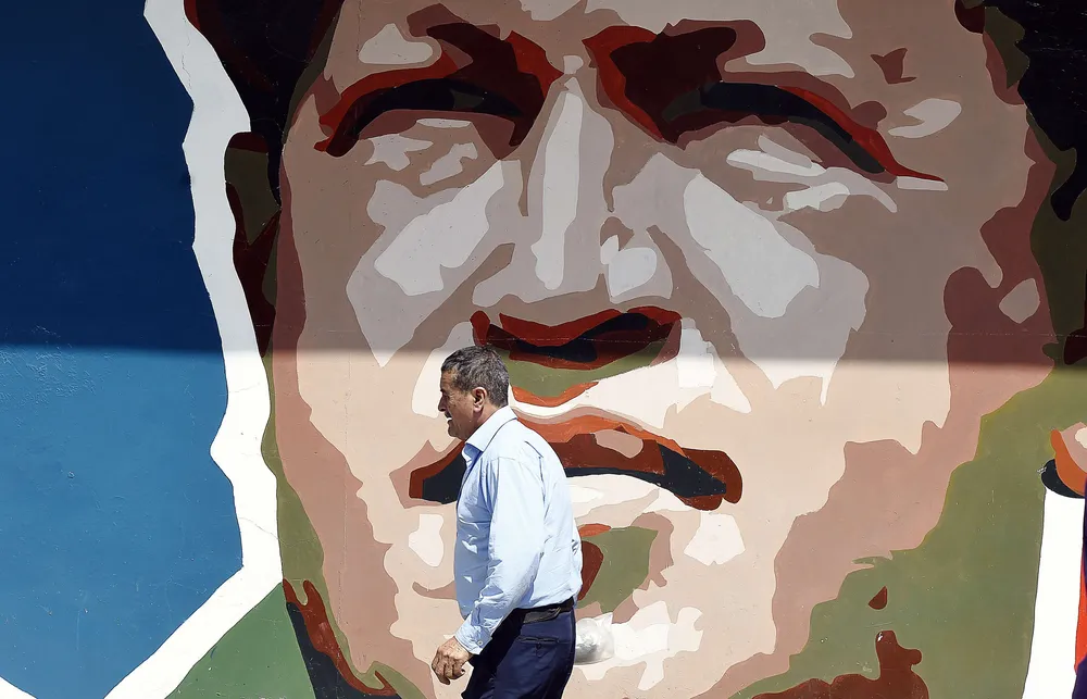 A man walks by a graffiti depicting late President Hugo Chavez in Caracas on November 13, 2015. The campaign for the legislative elections of December 6 in Venezuela started Friday in an environment marked by the arrest in the United States two relatives of President Nicolas Maduro, and the government and the opposition claiming favoritism. AFP PHOTO/JUAN BARRETO