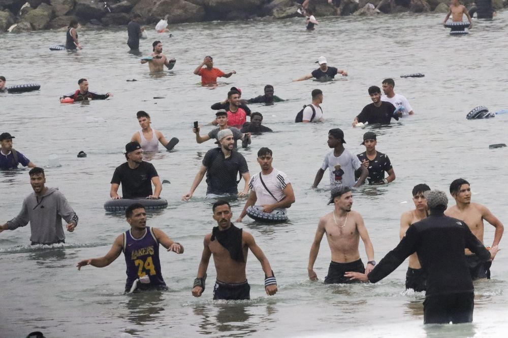 Un grupo de inmigrantes en la playa junto al paso fronterizo del Tarajal en Ceuta este viernes, donde se han registrado violentos enfrentamientos en los perímetros fronterizos durante su intento de acceder desde Marruecos hacia Ceuta y Melilla. 