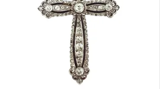 Lote 106. Cruz en oro 18 K blanco y amarillo con brillante central de 0,65 ct aprox. y 4 brillantes de 0,25 ct aprox. ubicados en cada extremo, decorada con dieciséis pequeños brillantes y sesenta y siete pequeños diamantes. 81 x 49 mm. Con detalles en esmalte negro, Peso bruto 16 gr.