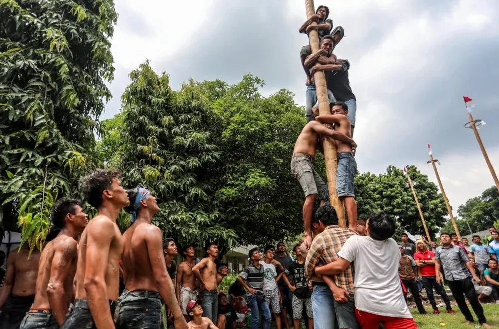 Trabajadores indonesios escalan palos de madera engrasados durante una competición con motivo del Día Internacional del Trabajador