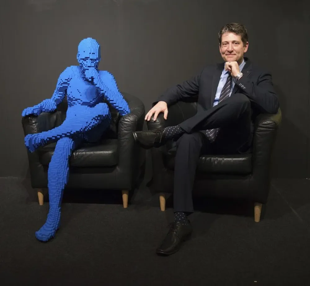 Artista estadounidense Nathan Sawaya, permanece sentado junto a una de sus creaciones en Alemania.