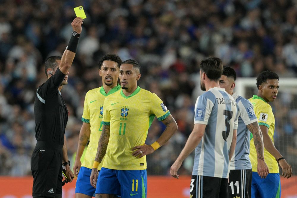 El árbitro colombiano Andrés Rojas le muestra la tarjeta amarilla a Nicolás Tagliafico de Argentina y a Raphinha de Brasil por las Eliminatorias