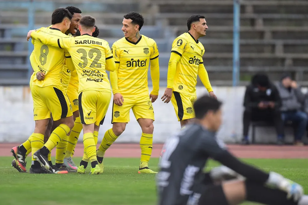 Abel Hernández y sus compañeros de Peñarol festejan su gol y Yonatan Irrazábal de Cerro lo sufre, por el Torneo Intermedio