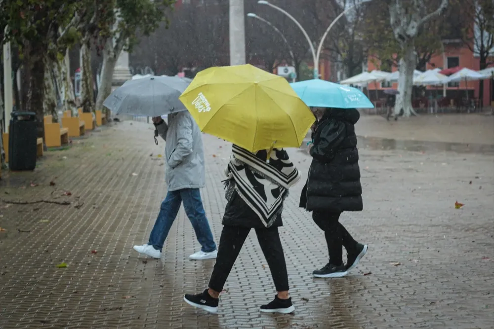 Tres personas se protegen de la lluvia con paraguas.