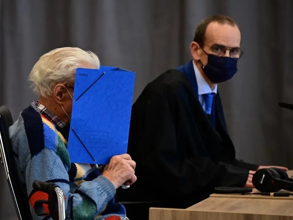 Josef Schütz tapándose el rostro con una carpeta