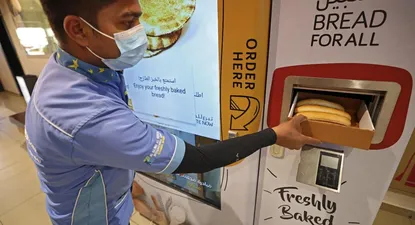 Un hombre recoge artículos de una máquina expendedora que reparte pan gratis, en Dubái.