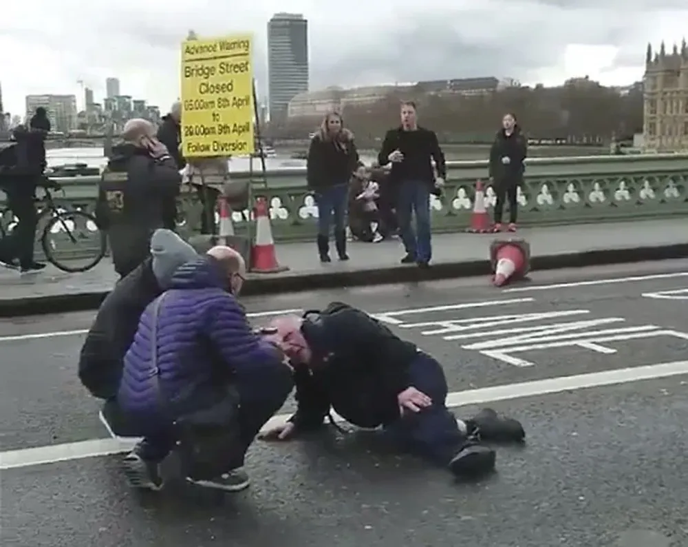 Personas atienden a un herido en el tiroteo en el Wetminster Bridge junto al Parlamento en Londres.